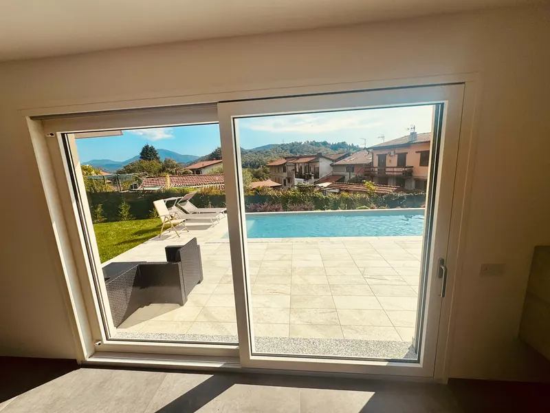 Grande porta finestra scorrevole bianca che si apre su una terrazza con piscina